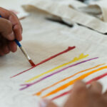 Detail shot of a hand painting a recycled bag with a brush and multiple colors.